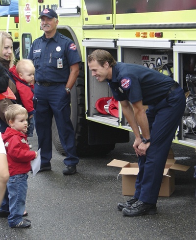 Firefighter Mike Hodo talks to a youngster while Firefighter Tom Donahue looks on from the background.