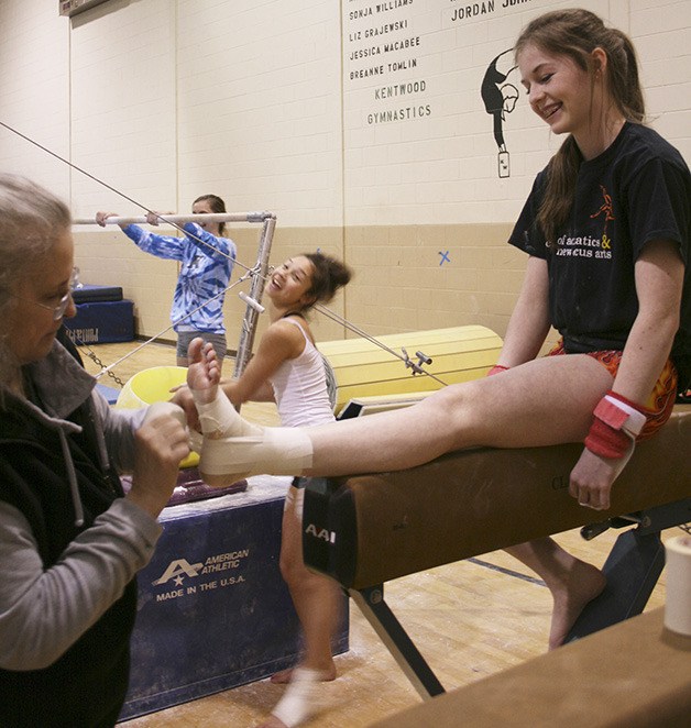 Zoe Krambule (right) laughs with her teammates at practice in the small Kentwood gymnasium while getting her injured left ankle taped by her coach