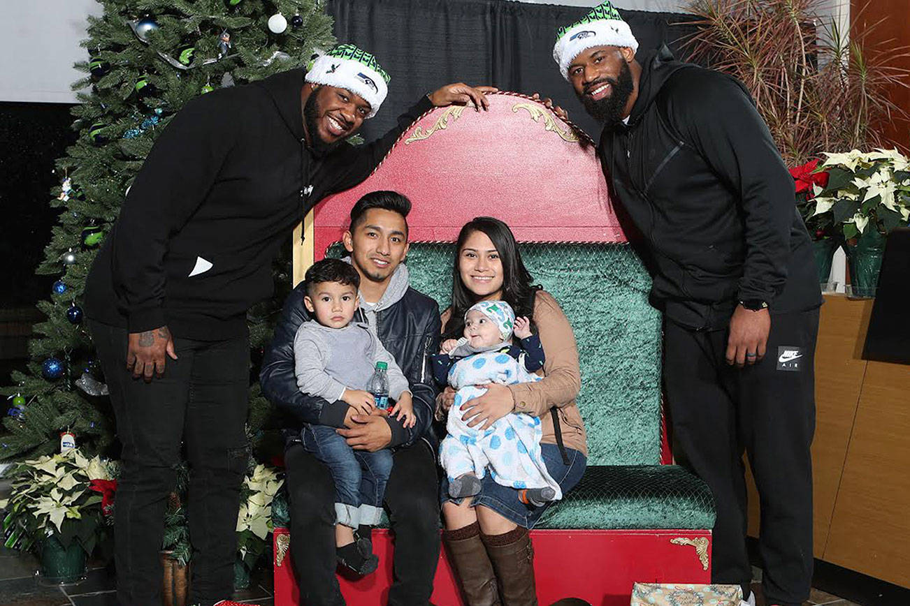 Quinton Jefferson and George Fant pose with a family during the holiday party Monday at the VMAC. Photo courtesy Seattle Seahawks