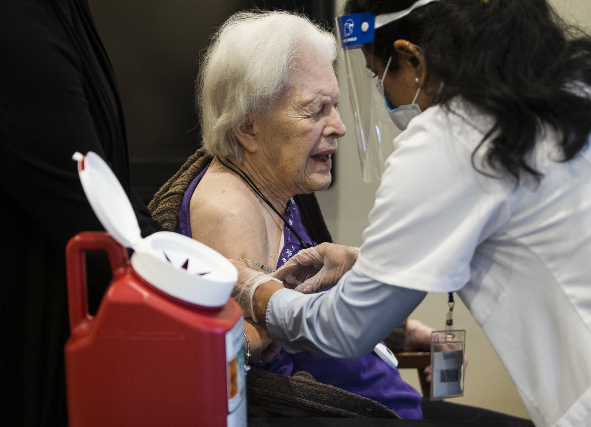 Jackie Hoernor, a resident at South Pointe Assisted Living, winces as she gets her Pfizer COVID-19 vaccination during a Walgreen’s Vaccine Clinic at South Pointe on Feb. 12 in Everett. (Olivia Vanni / The Herald)