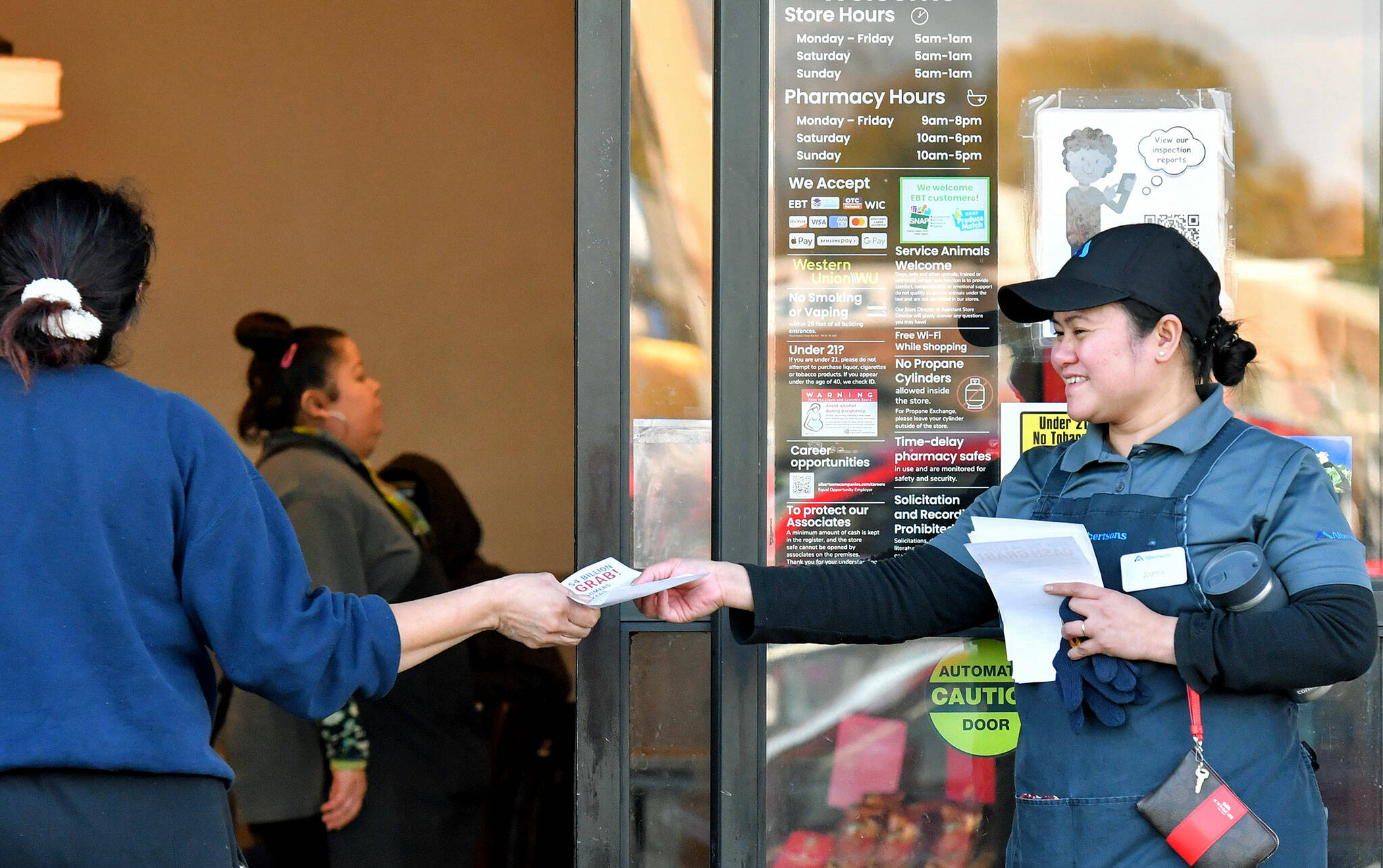 Joanne Fisher, right, a meat wrapper with the Marysville Albertsons, hands a leaflet to a shopper during an informational campaign on Wednesday. Fisher was one of less than a dozen grocery store workers handing out leaflets to shoppers about the proposed merger between Albertsons and Kroger. (Mike Henneke / The Herald)