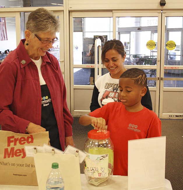 Baigeh Tucker puts money into a jar during the Mayors Day of Concern in Covington for the Hungry on Saturday at Fred Meyer as his mother