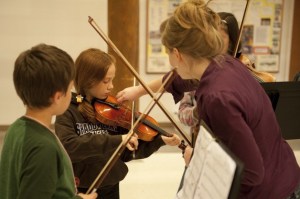 Sarah Burwell (right) assisting violinists Avery Black (left) and Daria Cawthorn (center).