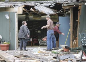 Nikki Devoni stands amid the rubble of the part of her mother’s house that was struck last Friday by an airplane that crashed into the home’s yard. With her Saturday are family friends John and Jack Clark