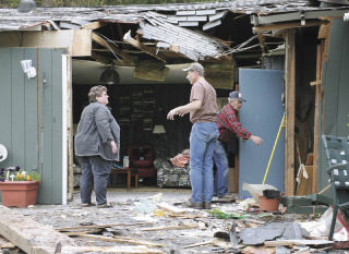 Nikki Devoni stands amid the rubble of the part of her mother’s house that was struck last Friday by an airplane that crashed into the home’s yard. With her Saturday are family friends John and Jack Clark