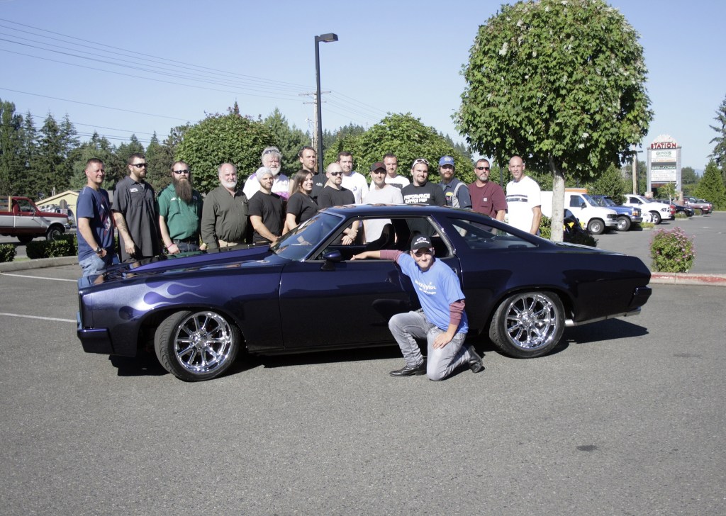 Damian Taylor kneels in front of his car with everyone who helped with the car renovation