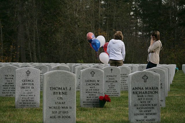 Two women stand in the distance after placing flowers and balloons at a grave site at the Tahoma National Cemetery Friday. Following the ceremony, many placed flowers on loved one&rsquo;s graves.