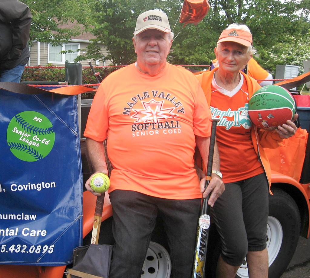 Photo by DAnn Tedford                                 Senior Softball Manager and Coach Gene Tuffs holds a softball, a slow pitch bat and a tennis racquet signed by Billie Jean King. Judi Kloss, an assistant coach, handed out basketballs to those along the Maple Valley Days parade route.