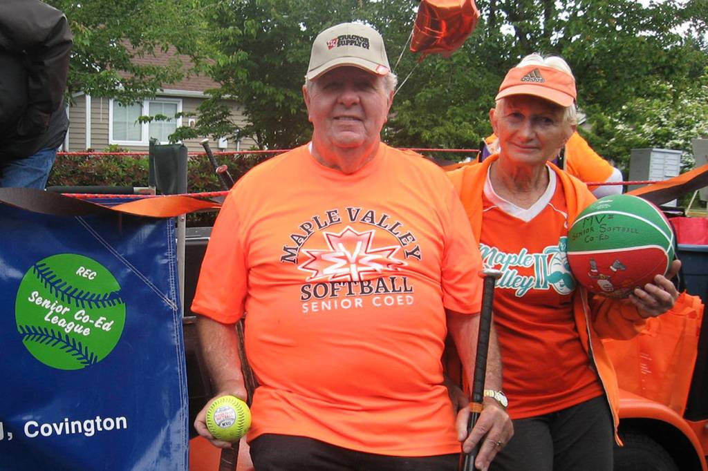 Photo by DAnn Tedford                                 Senior Softball Manager and Coach Gene Tuffs holds a softball, a slow pitch bat and a tennis racquet signed by Billie Jean King. Judi Kloss, an assistant coach, handed out basketballs to those along the Maple Valley Days parade route.