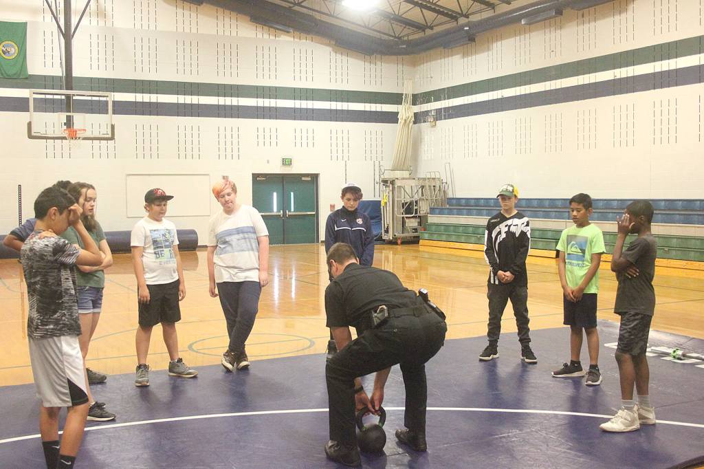 Covington Police Chief Andrew McCurdy shows students how to properly lift a kettle ball weight at the Barbells and Badges summer camp.
