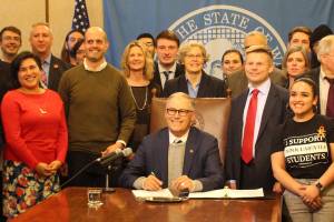 Gov. Jay Inslee signs the first bill of the 2020 legislative session into law. On the right stands the bills primary sponsor, Sen. Jamie Pedersen, D-Seattle, who is wearing a red tie. Photo by Cameron Sheppard, WNPA News Service